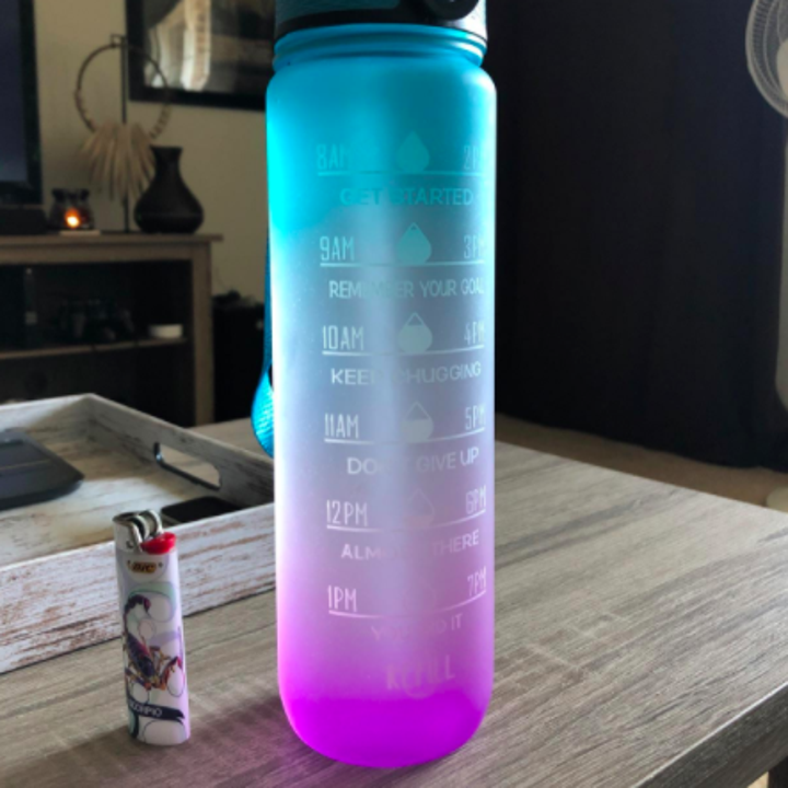 The Giotto Leakproof BPA Free Drinking Water Bottle with Time Marker &amp; Straw in a customer's home. A lighter stands beside it showing the difference in size.
