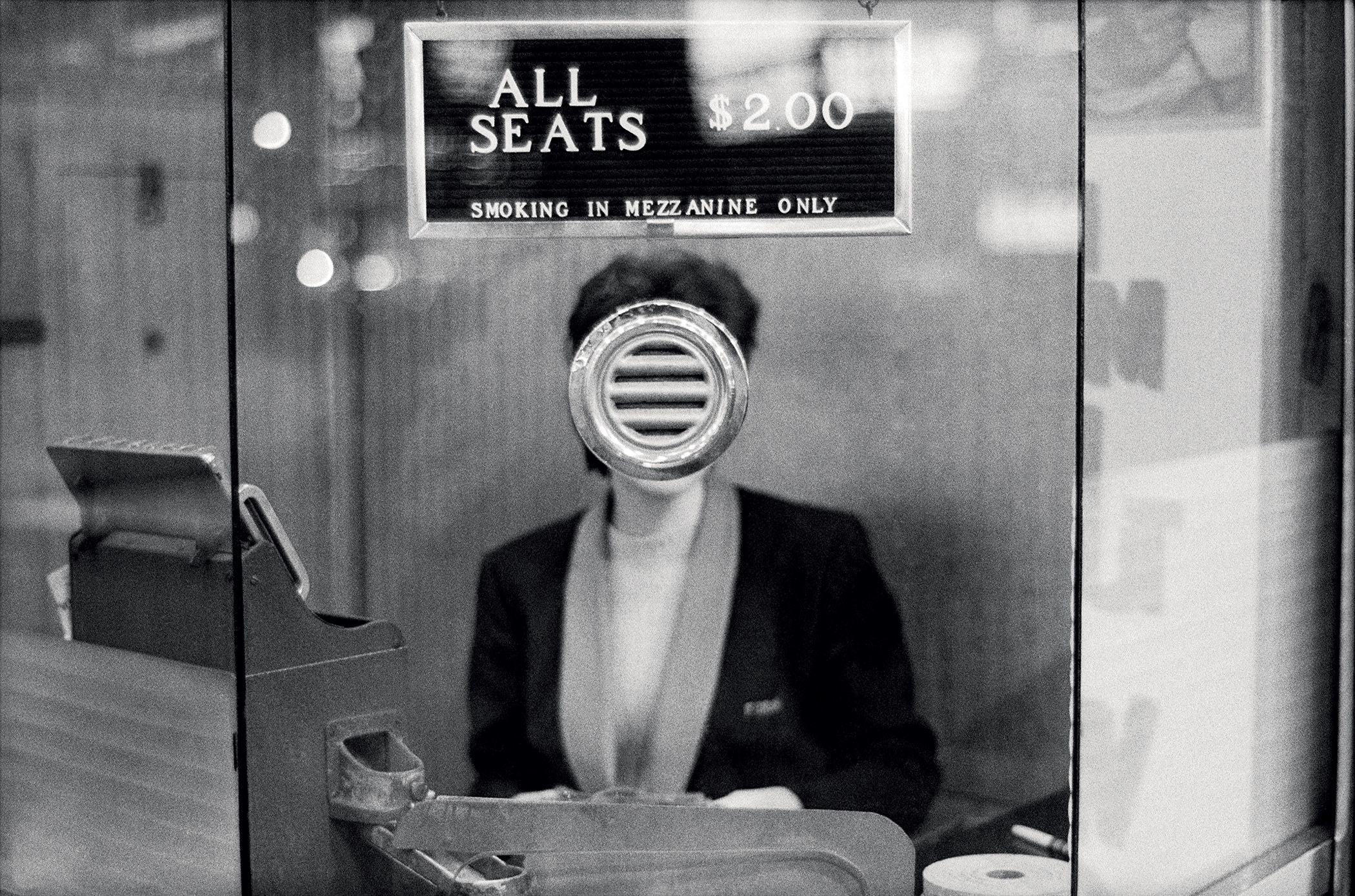 A woman&#x27;s face is obscured as she sits in the ticket booth at a movie theater