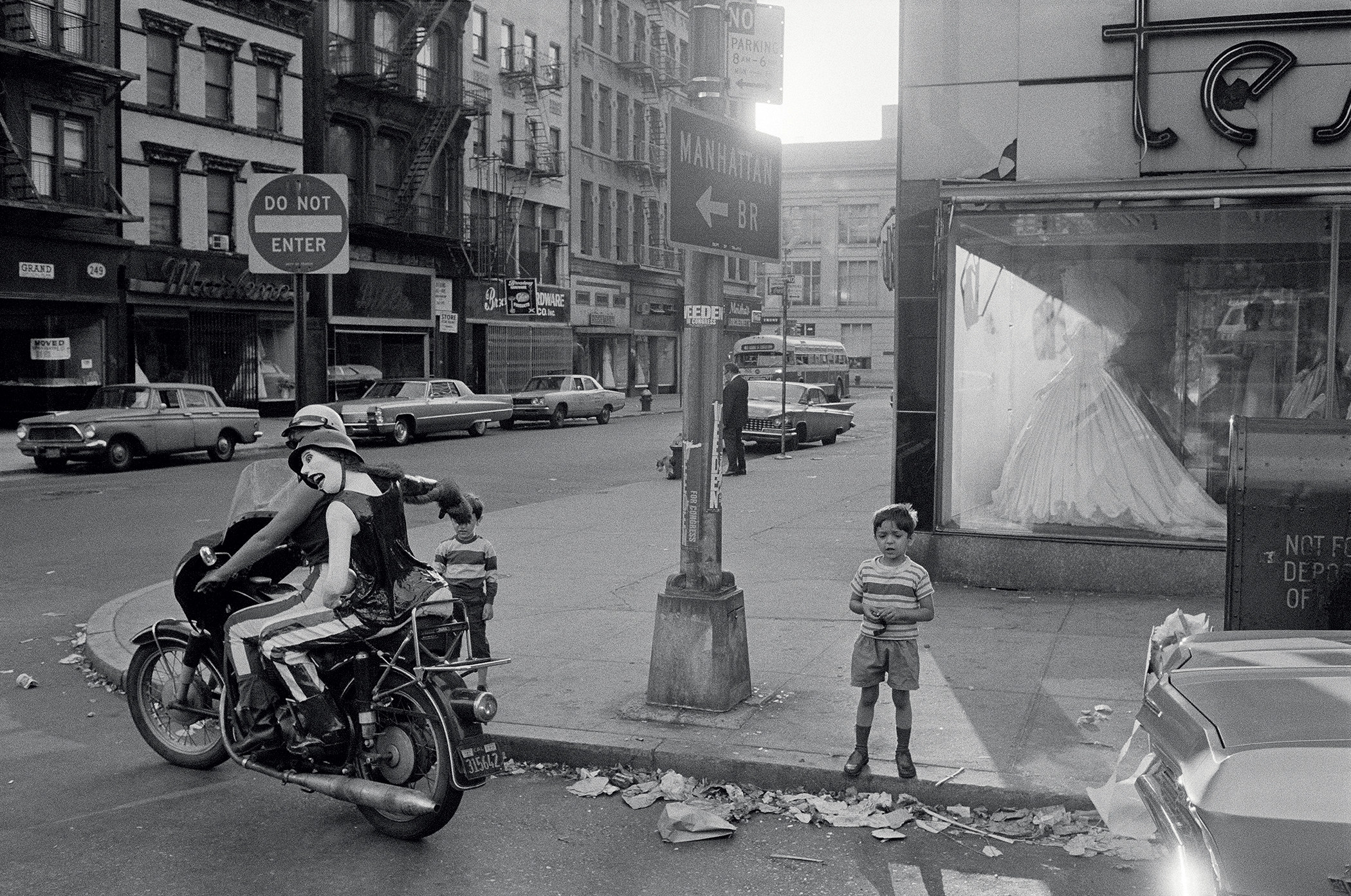 Two boys standing on the sidewalk watch a motorcycle drive by