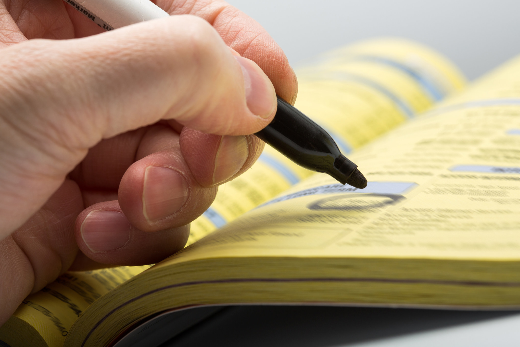 A stock photo of a someone circling a number in the phone book with a black marker.