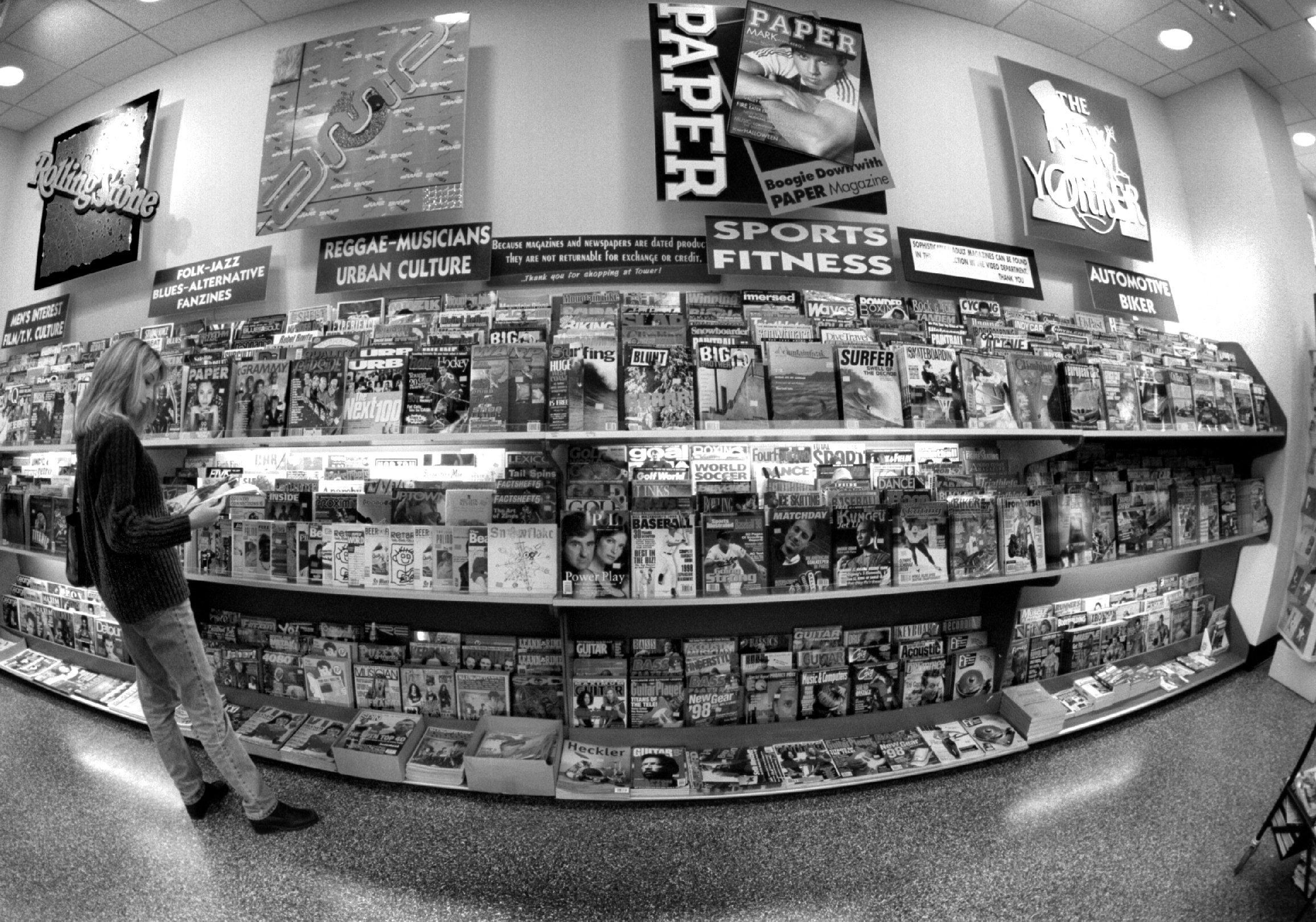 A fish-eyed lensed black and white photo of the magazine section at Tower Records in 1998.