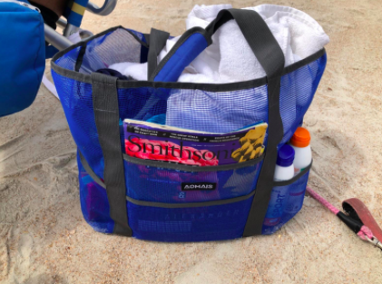 Reviewer&#x27;s blue beach tote stocked with sunscreen and towels on the sand