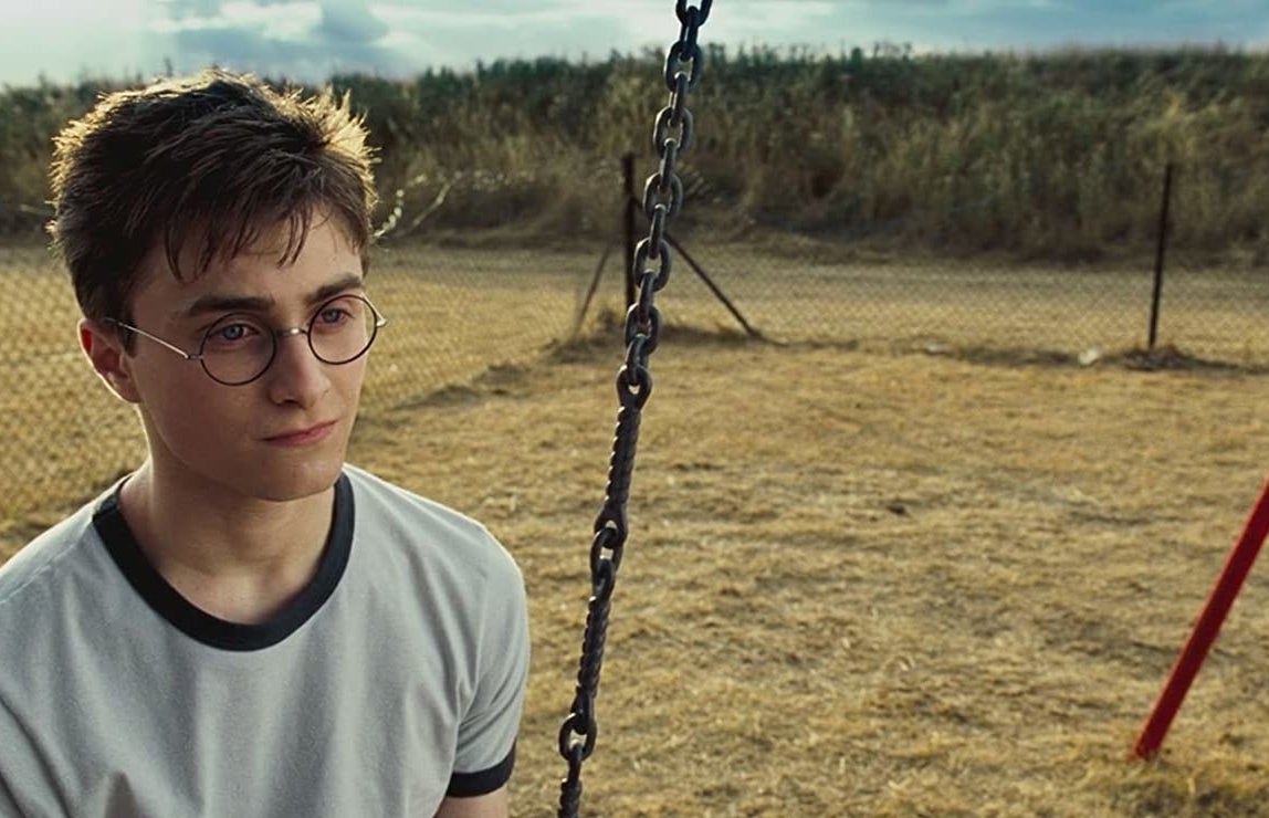 Daniel Radcliffe as Harry Potter sits on a swing looking glum