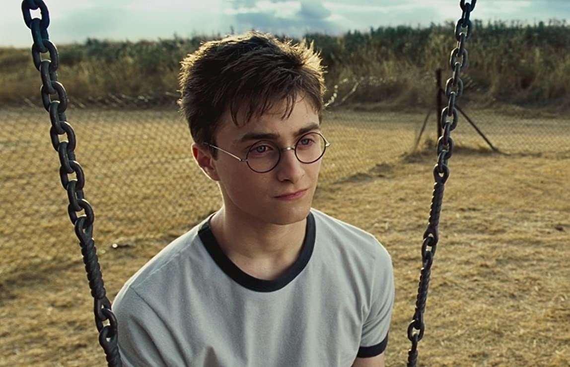 Daniel Radcliffe as Harry Potter sits on a swing looking glum