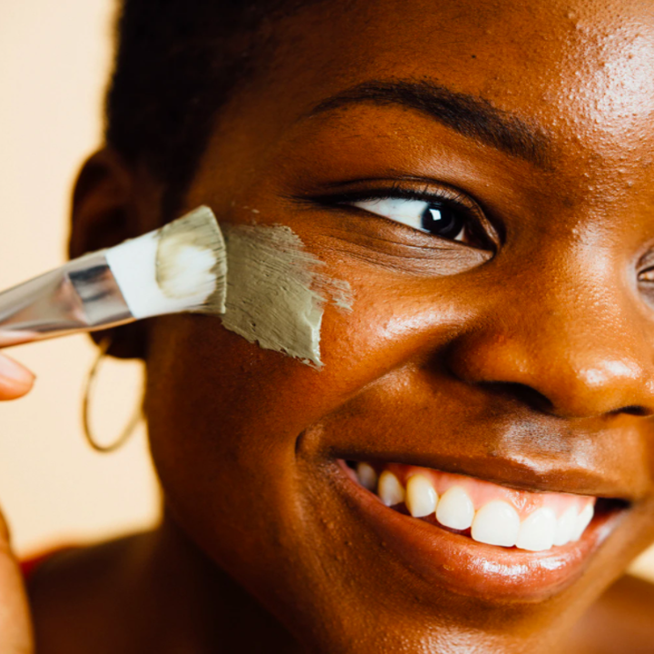 A person applying the dead sea mud mask to their cheek with the spatula