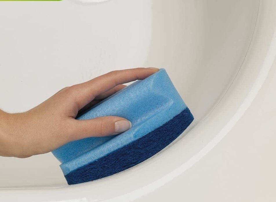 A person scrubbing the corner of a bathtub with the bathroom scrubber