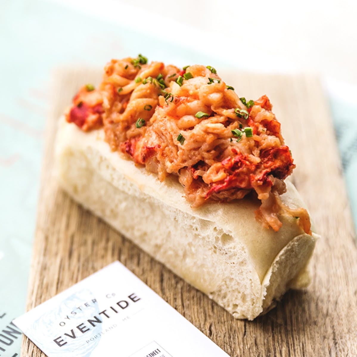 A soft bun stuffed with lobster meat in brown butter on a wooden tabletop.