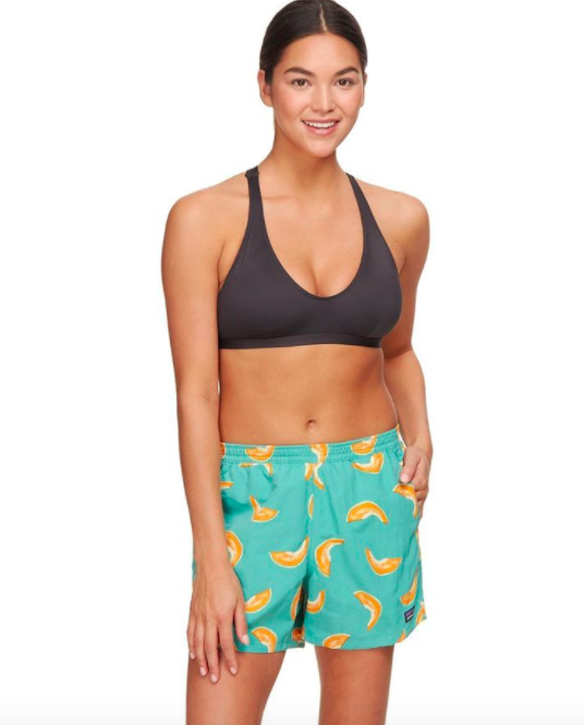 Model wears blue and yellow printed board shorts with a black bikini top