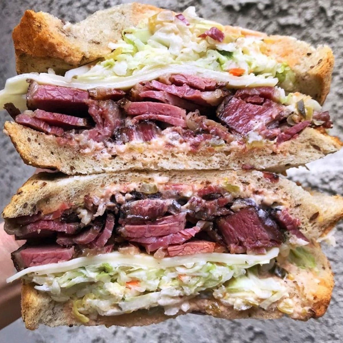 Two halves of a Langer&#x27;s Original #19 on Jewish Rye bread, stuffed with pastrami, coleslaw, and mayo.