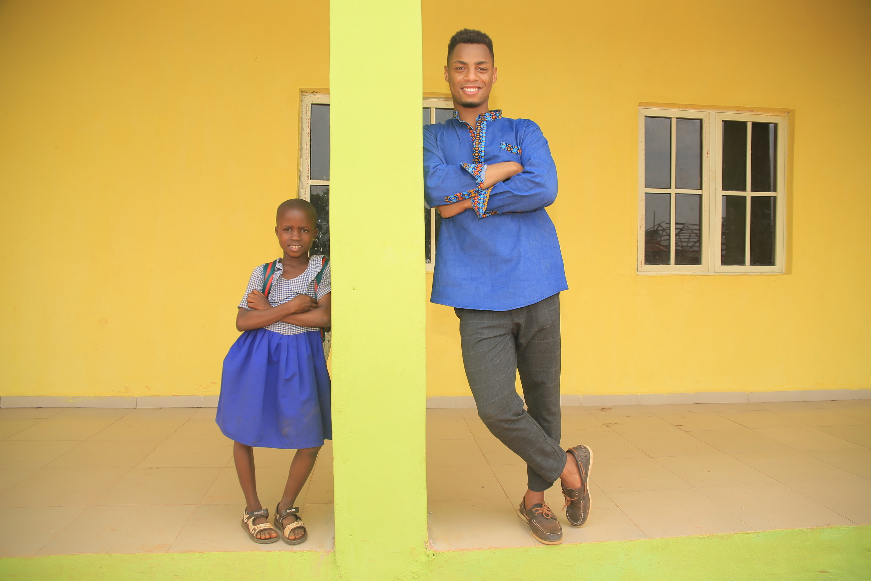 A young child (left) and Uyi Omorogbe (right) lean against a yellow pillar