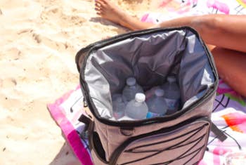 Reviewer shows open white cooler of water bottles while sitting on a beach blanket 
