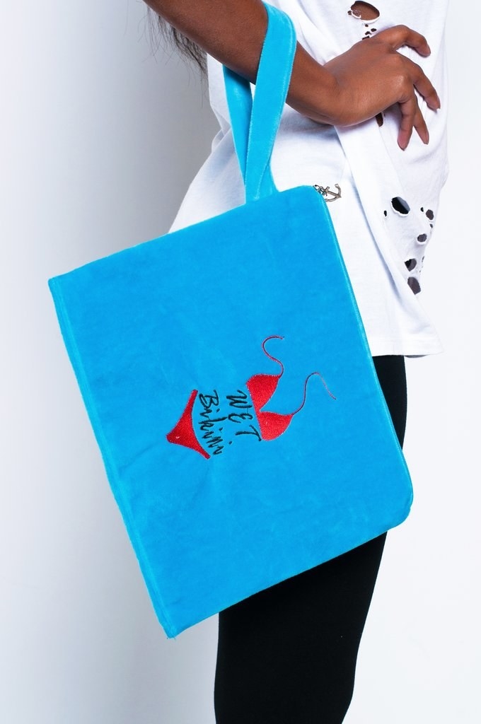 A model holding the blue bag that reads &quot;wet bikini&quot; with an embroidered bikini on it