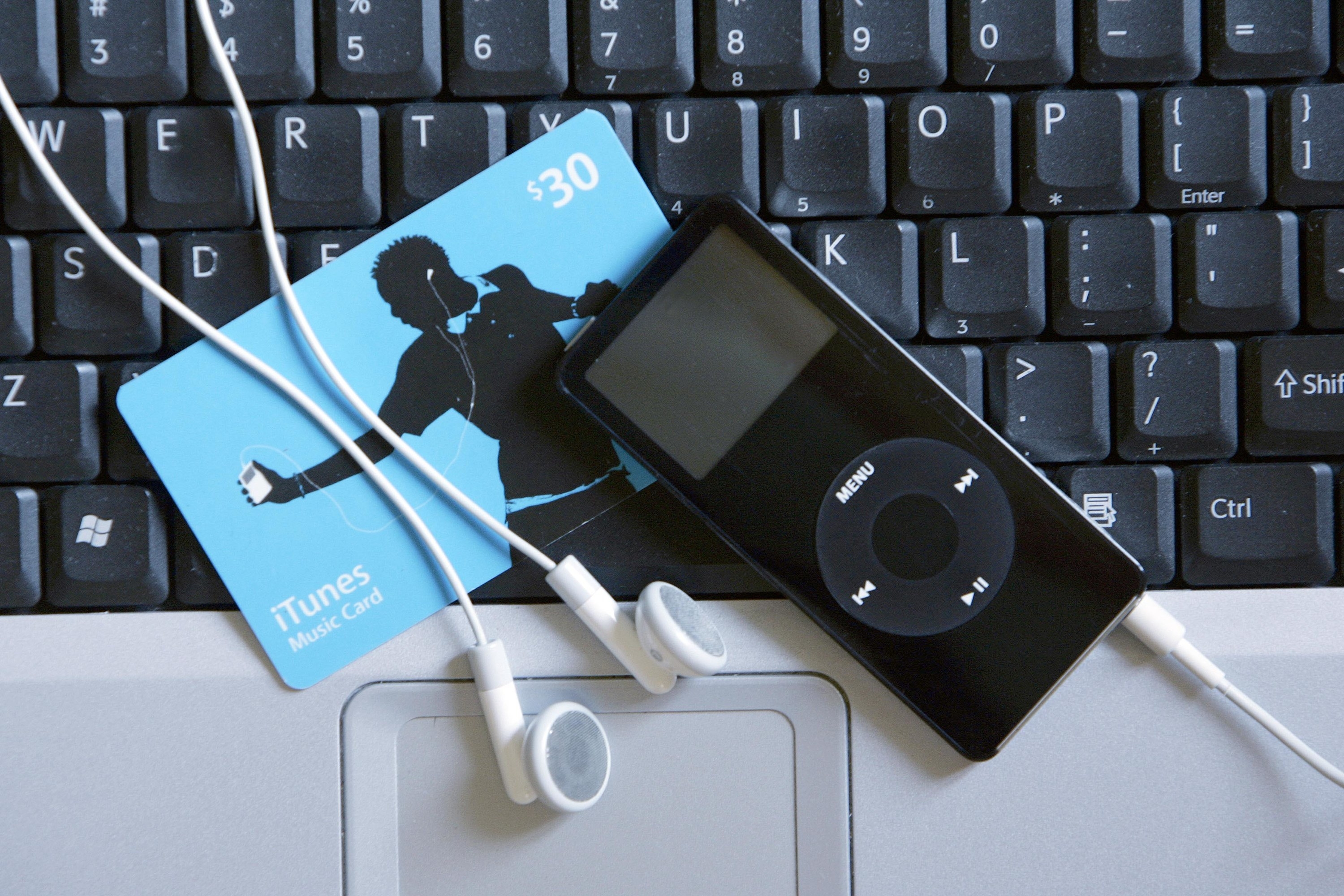 Picture of an iPod Nano, an iTunes Music Card, and iPod headphones on top of the keyboards of Macbook. 