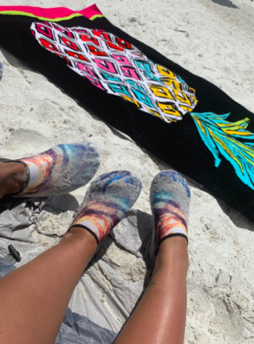 Reviewers wear rainbow-colored water shoes while sitting on a beach blanket