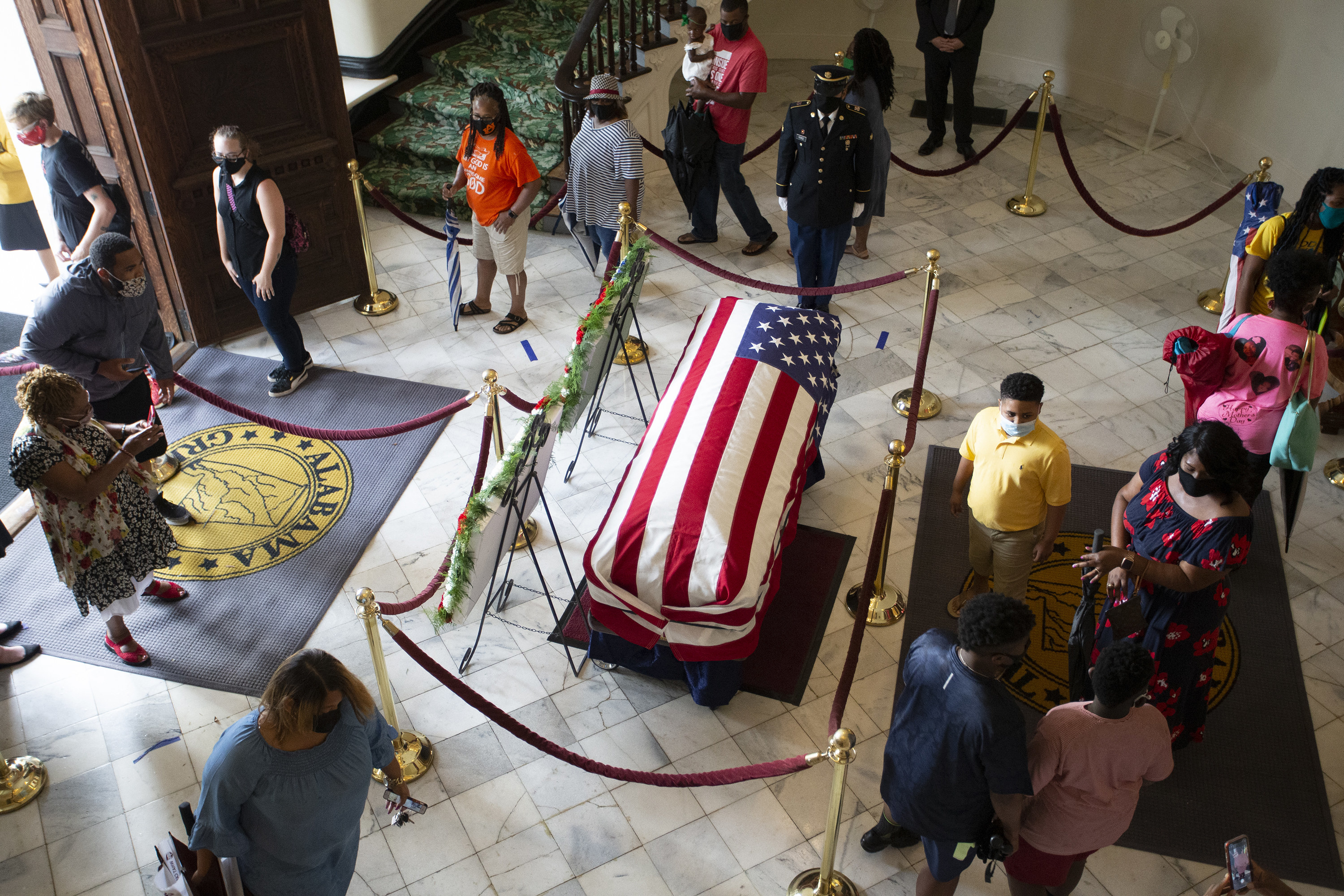 Visitors wearing masks walk around a casket, which is covered by a US flag and cordoned off by velvet rope barriers