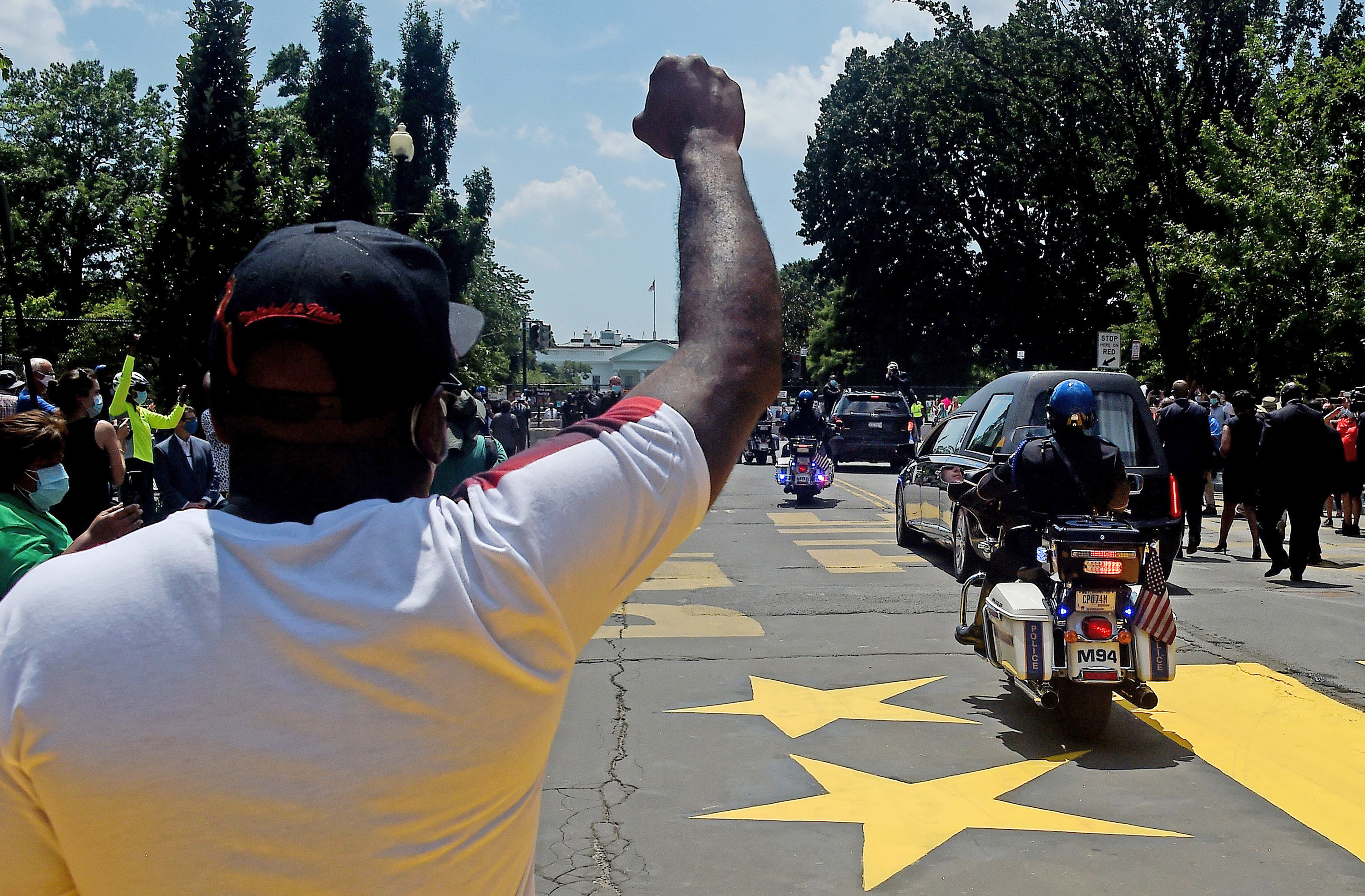 A Black man raises his fist as the hearse carrying Rep. John Lewis&#x27;s body drives on