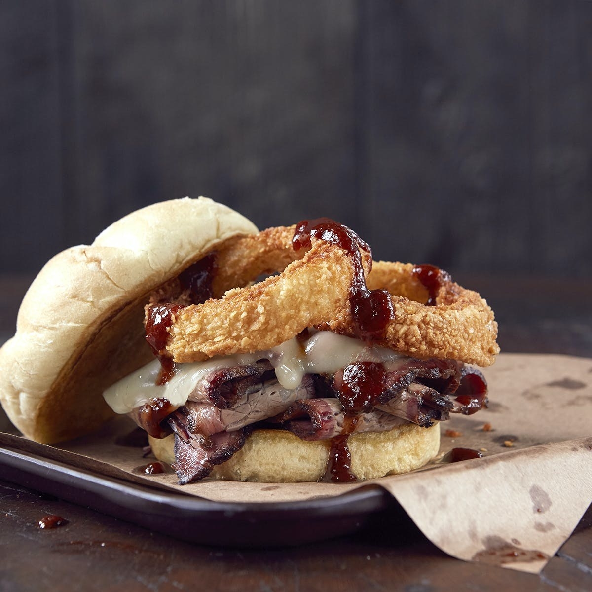 A Joe&#x27;s Kansas City BBQ brisket sandwich with Provolone and onion rings on a roll.