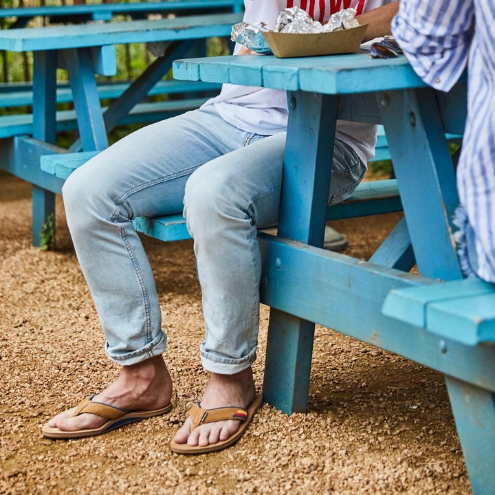 Model wearing tan-colored sandals with rainbow-pattern accent on strap