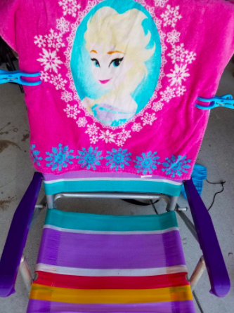 reviewer's blue clamps holding down a pink beach towel on a striped chair