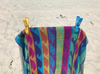 Reviewer uses a yellow and blue clamp to hold down a colorful towel on a beach chair
