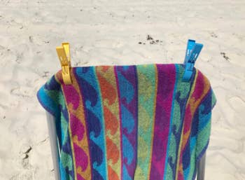 Reviewer's yellow and blue clamp to hold down a colorful towel on a beach chair
