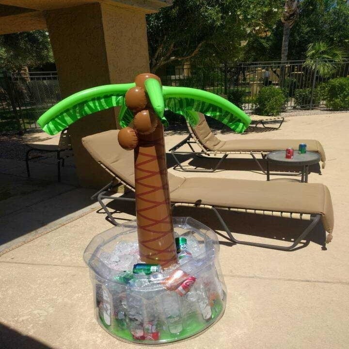 Inflatable palm tree cooler with bright green leaves, a brown trunk, and a clear plastic base filled with ice and drinks
