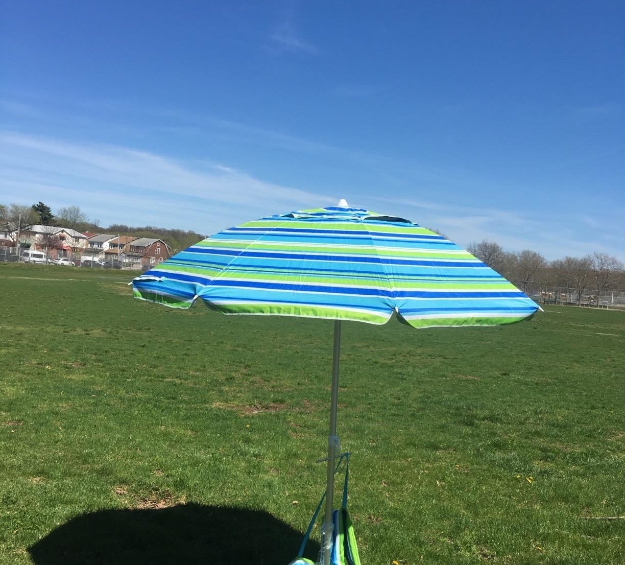 A large blue and green striped umbrella stuck into the grass