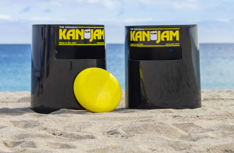 Two black targets with slots that say &quot;Kan Jam&quot; with a yellow frisbee on the sand