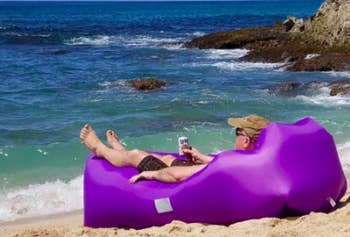 Reviewer sits in purple inflatable lounger while drinking a beer on the shore