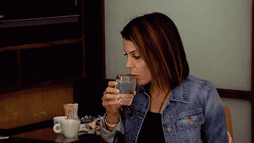A woman is holding a glass of water, and her hand is shaking. She is having a hard time drinking it.