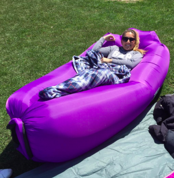 Reviewer sits in same inflatable lounger with a blanket in a grassy area