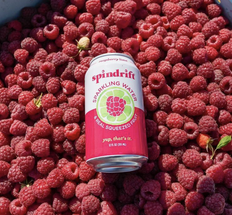 A can of spindrift raspberry lime water lies on a bed of raspberries in the sunshine.