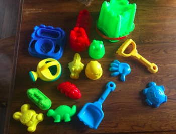 A reviewer's set of red, yellow, blue, and green toys with a green sand pail on a hardwood floor