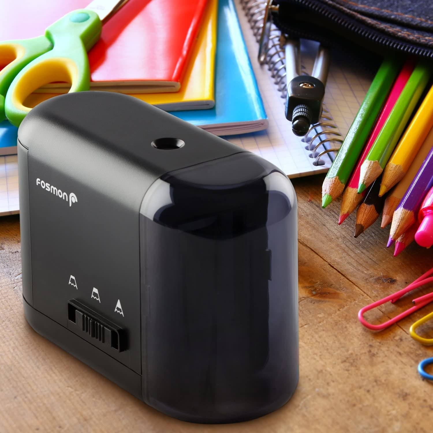An electric sharpener beside sharpened pencils notebooks and other school supplies