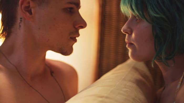 A young man and woman sit face-to-face, only a pillow between them