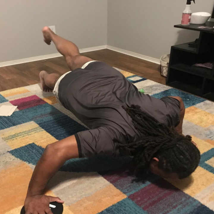 A reviewer performs one-legged sliding pushups on their carpet with the core sliders