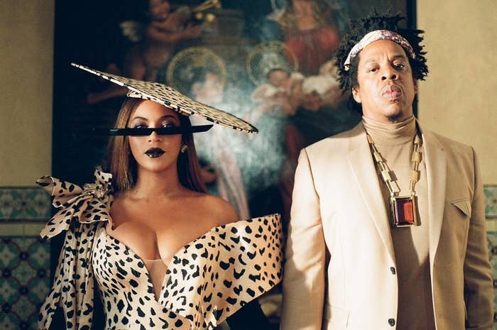 Beyoncé wears an animal print dress and hat next to her husband, Jay-Z, who wears a tan-colored suit jacket and turtleneck