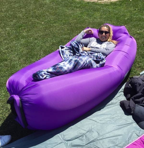 A reviewer laying down on the purple inflatable lounger