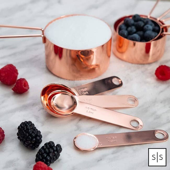 The cup and teaspoon/tablespoons measuring cups in rose gold displayed on a table. 