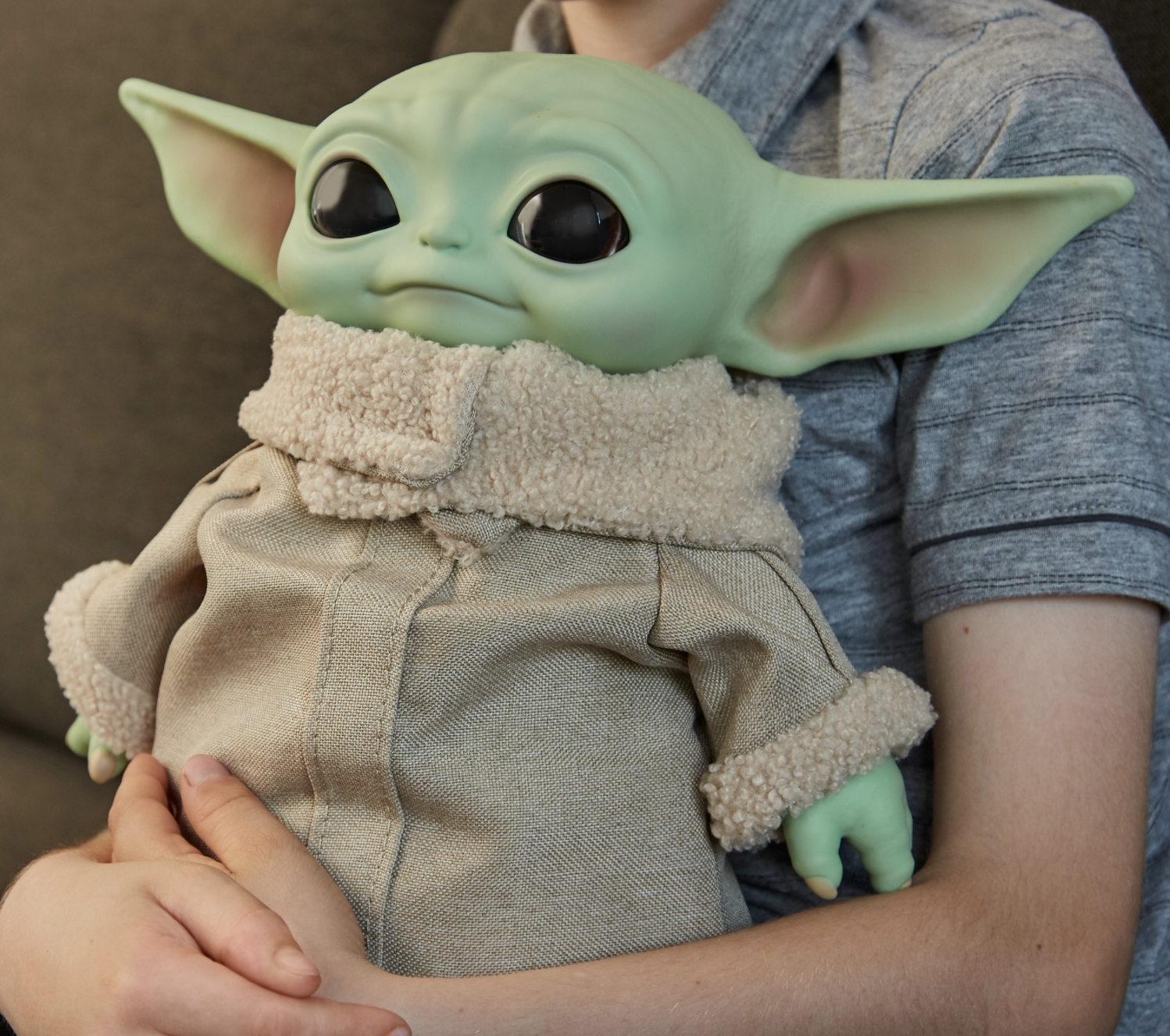 a model holding the baby yoda plush on their lap