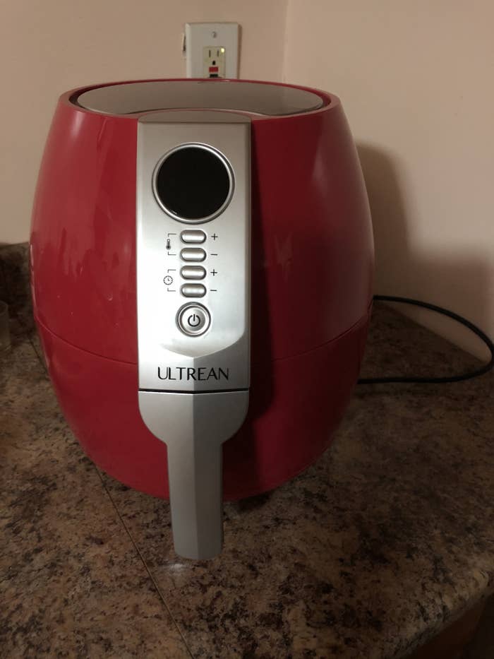 A red air fryer on a counter top. The air fryer has a handle for pulling out the frying chamber