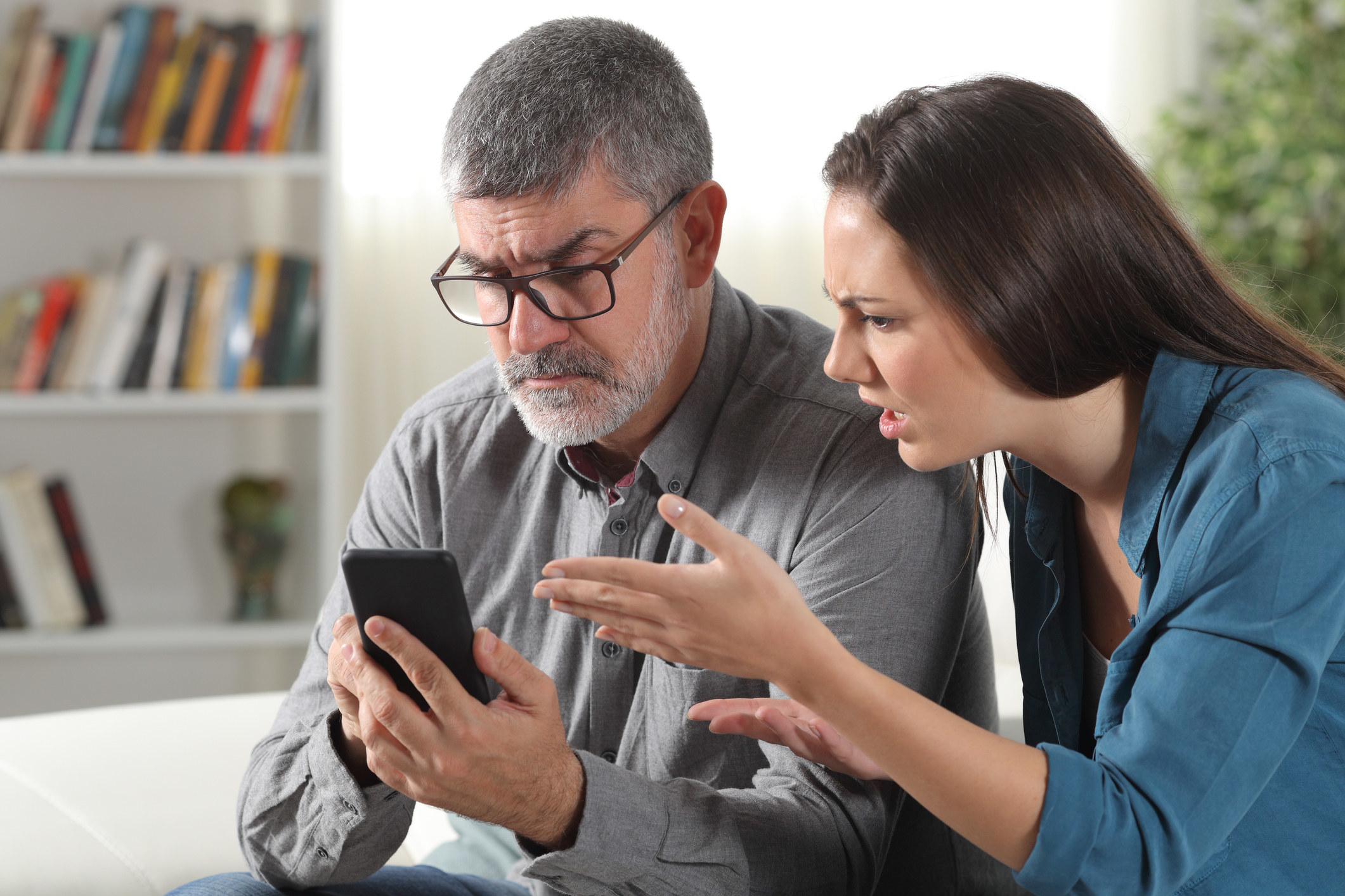 A woman looking over her father&#x27;s shoulder at his phone in anger