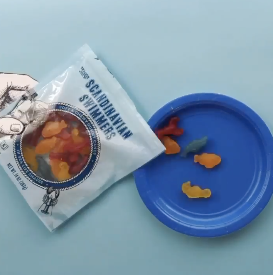 A bag of gummies shaped like ocean creatures are being poured out onto a paper plate.