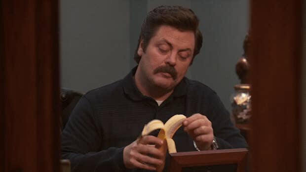 A man with a mustache is unpeeling a banana.