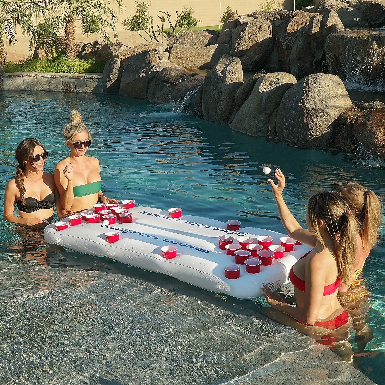 Four models play beer pong on the floating rectangular rafter with cup holders for solo cups
