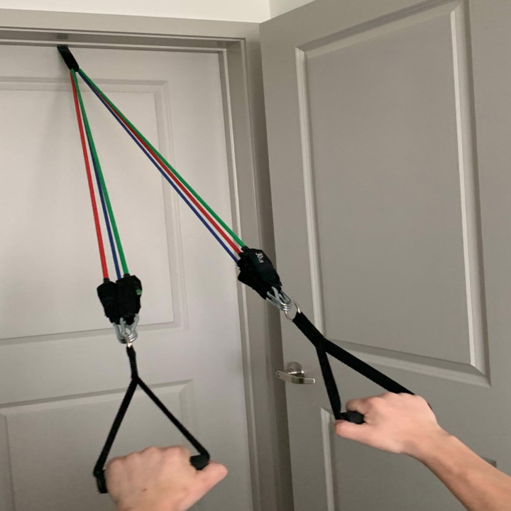 A reviewer demonstrating the resistance bands anchored to their door, with a handle in each hand
