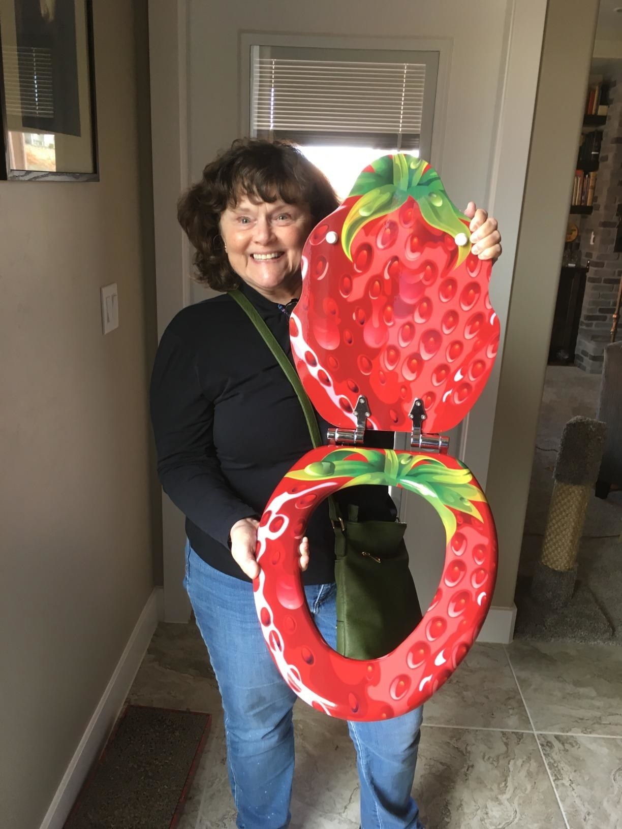 reviewer poses next to strawberry toilet seat. yes, the lid is shaped like a strawberry and the bottom part of shaped like a regular toilet seat but with a strawberry pattern