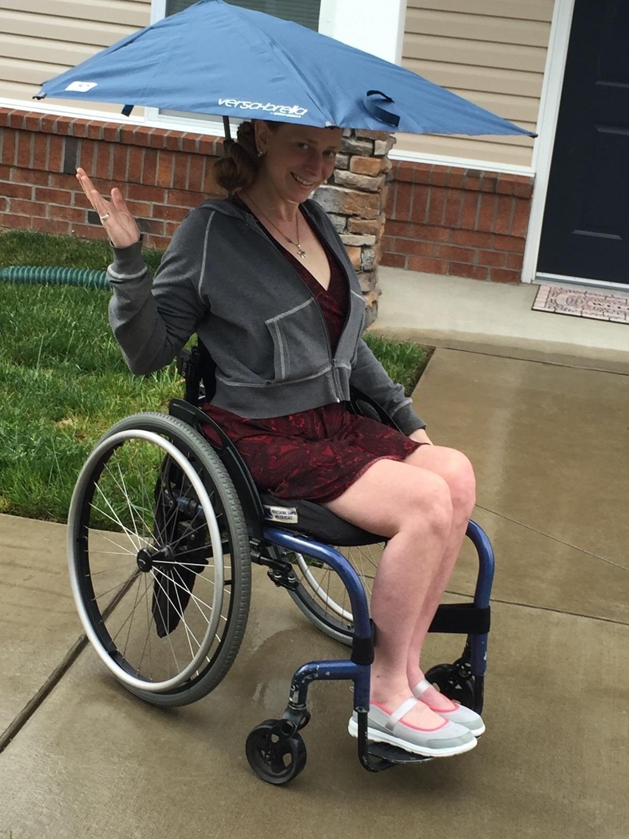 A reviewer showing off the umbrella that is clipped to their wheelchair