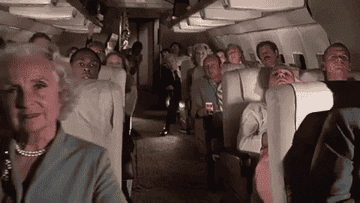 GIF of an airplane filled with people leaning into the aisle and peering into the camera.