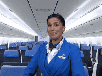 GIF of a flight attendant on an empty airplane throwing her arms in the air in excitement 